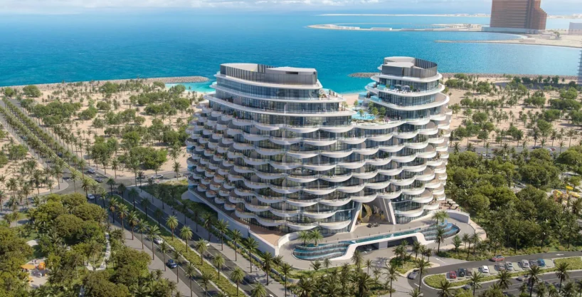 "Aqua Arc," a pair of curved, modern buildings, stands near a coastline with blue water and lush greenery.